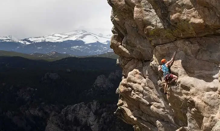 Rock climber scaling cliff with mountain view