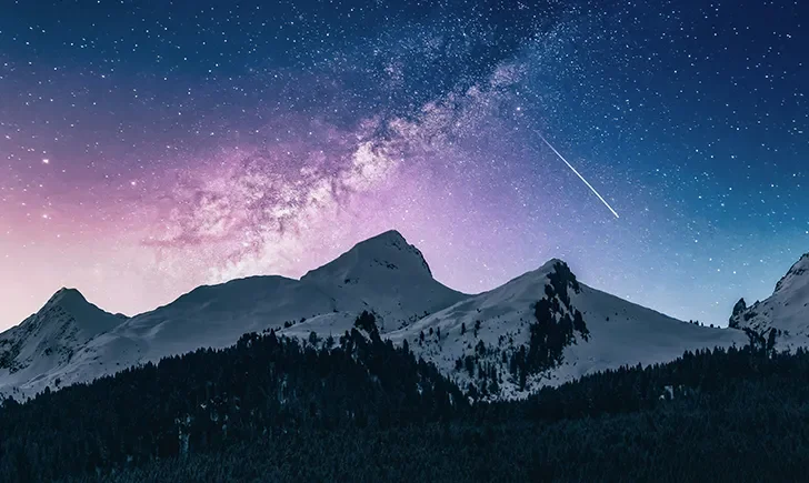 Starry night sky over snowy mountains